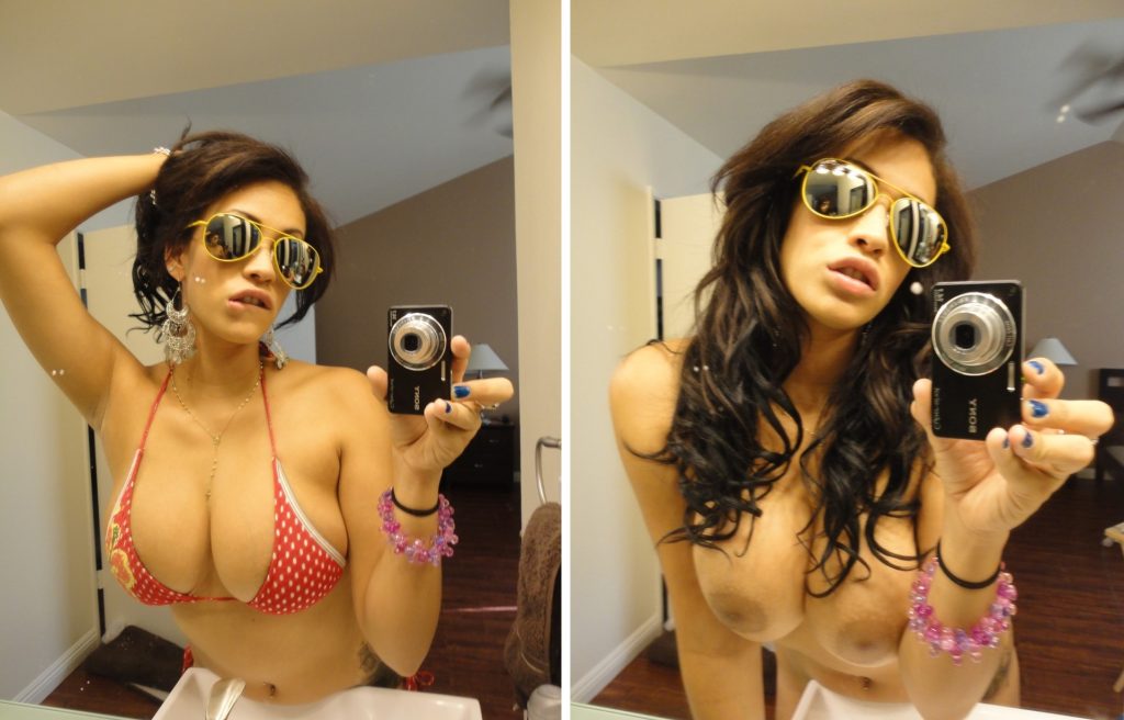 Real babe with big tits taking selfie with sunglasses on and biting her full lips.